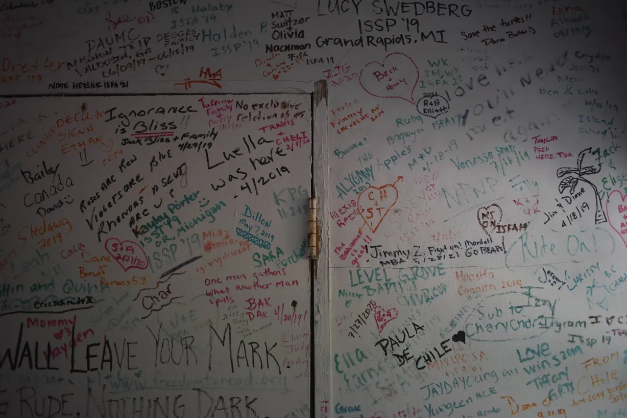 Photo of a cabin door and wall covered in visitors’ signatures and messages, with “Leave your mark” written large