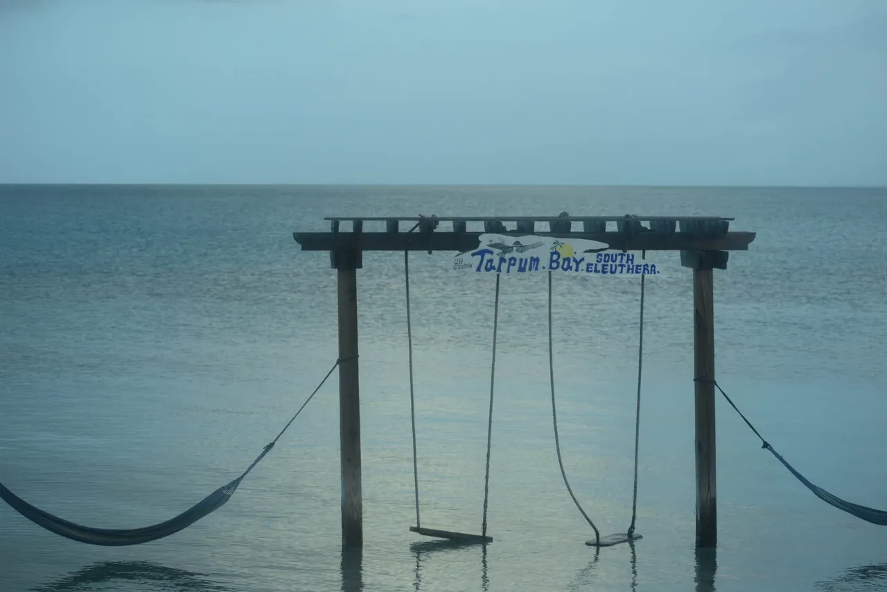 A wooden dock with swings over calm evening water, signed “Tarpum Bay, South Eleuthera”