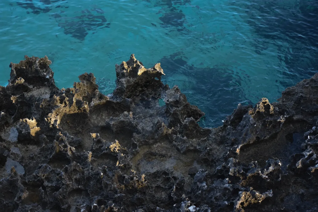 Close-up of dark volcanic rock against turquoise ocean water