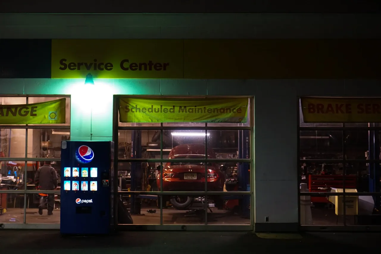 Night photo of an auto service center, a red car visible on a lift through the garage window