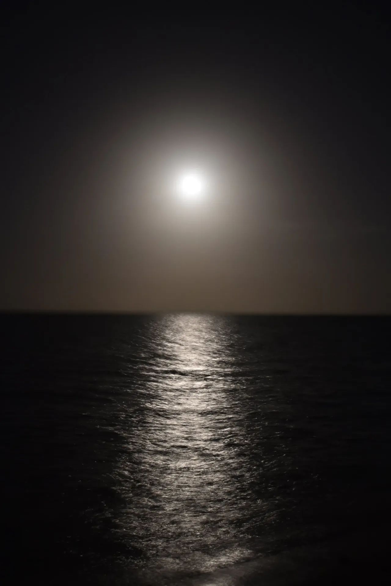 The moon reflecting a path of light across dark ocean water at night